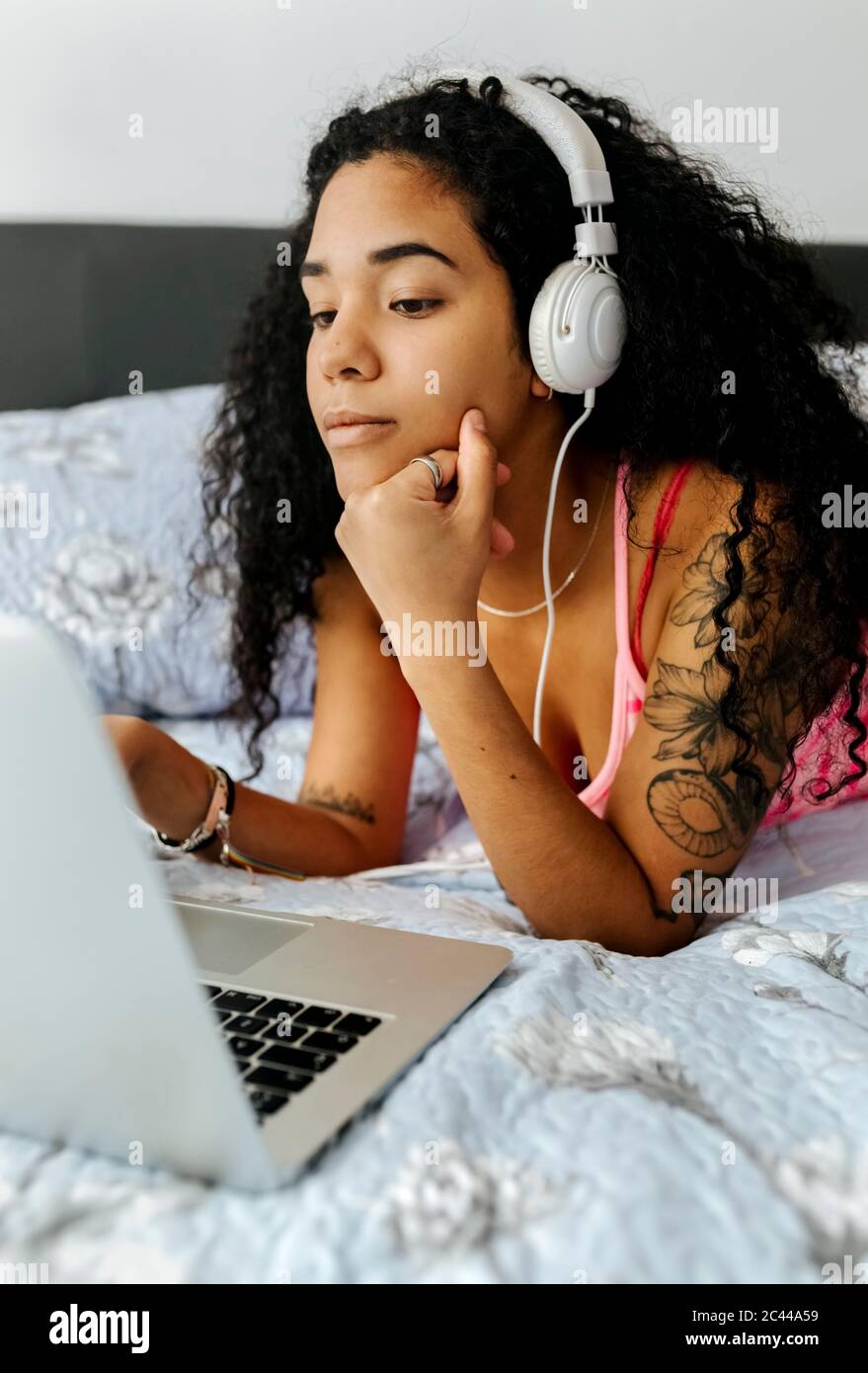 Beautiful young woman lying in bed at home wearing headphones and using