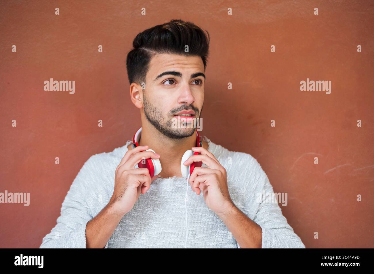 Young handsome man holding headphones against brown wall Stock Photo
