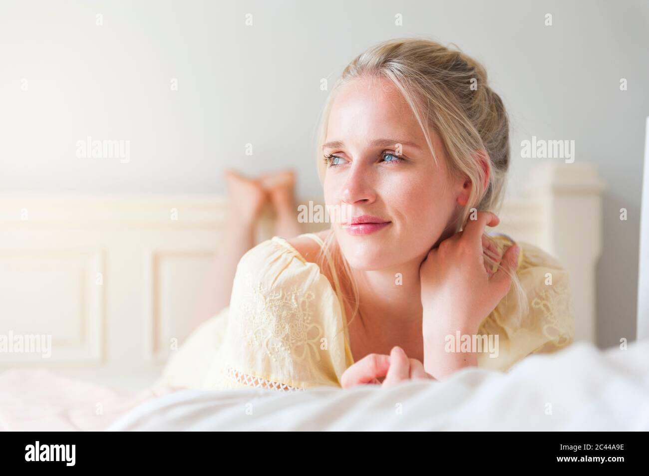 Portrait of smiling blond woman with blue eyes lying on bed Stock Photo