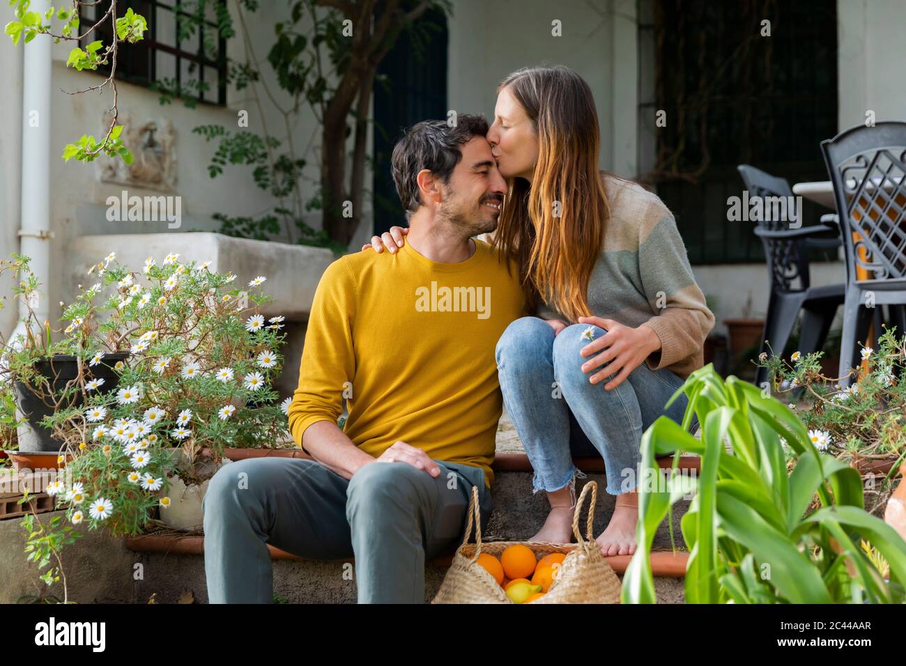 Romantic woman kissing on boyfriend's forehead while sitting over steps against farmhouse Stock Photo