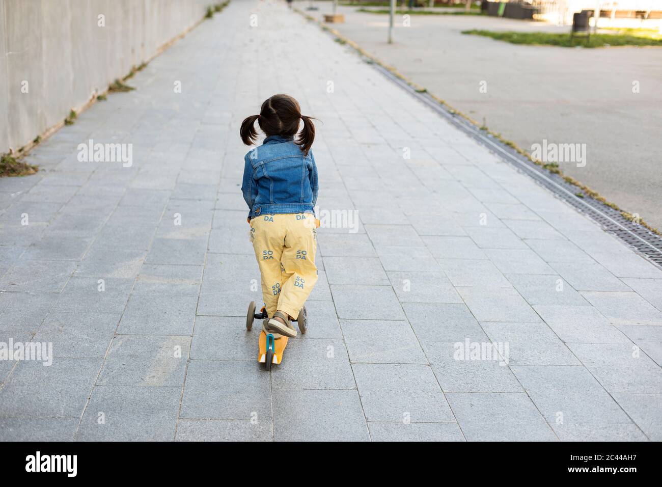 Back view of little girl with scooter on pavement Stock Photo