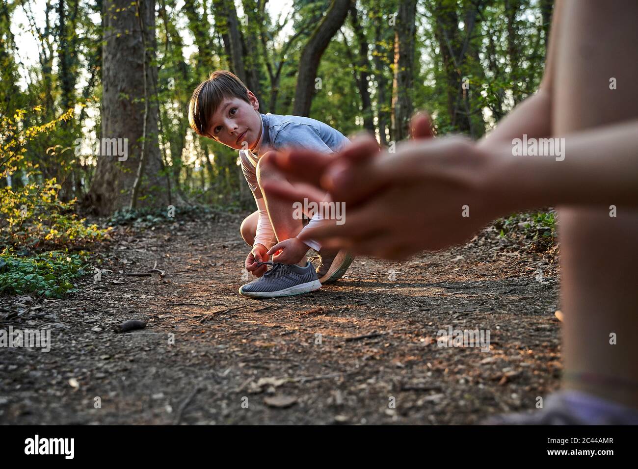 Boy tying his shoelace while looking at sister in forest Stock Photo