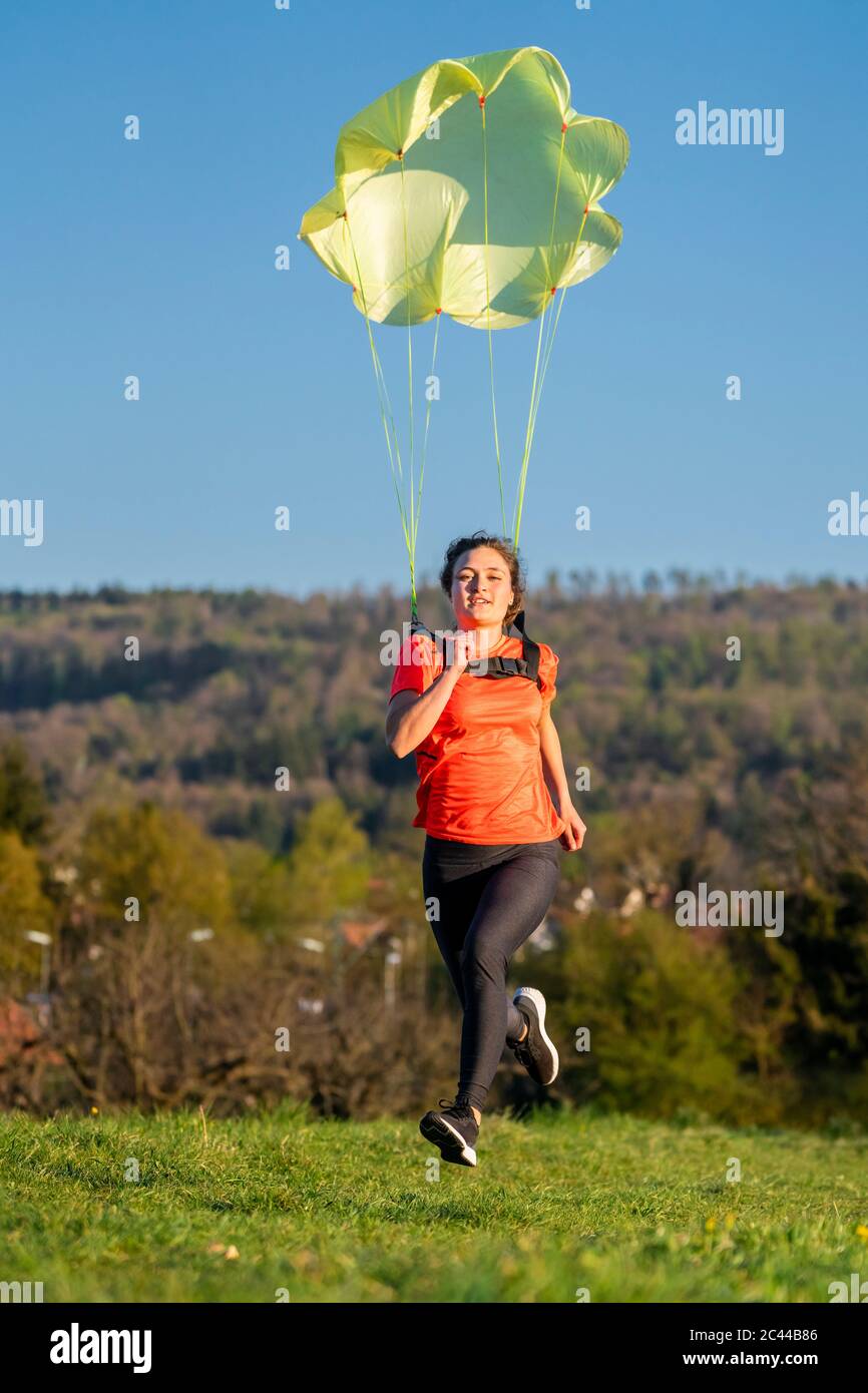 Full length of young woman sprinting with parachute on grass against clear sky Stock Photo