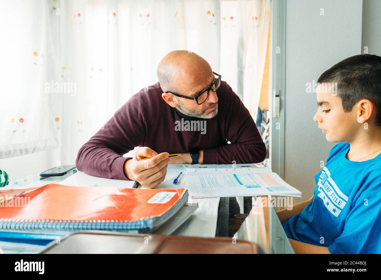Father explaining son sitting at desk during homeschooling Stock Photo
