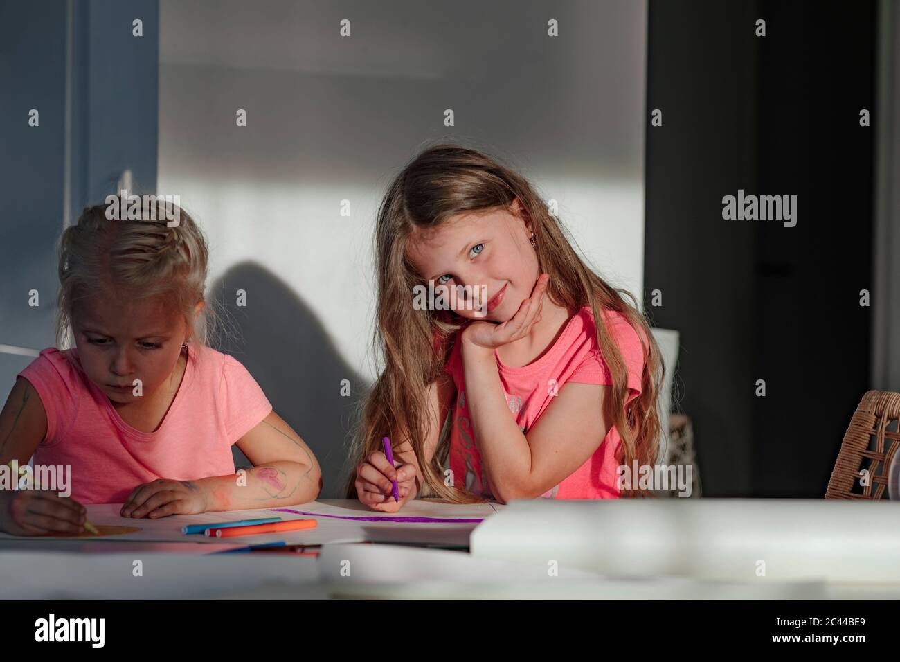 Happy girl sitting with sister coloring on paper at home Stock Photo