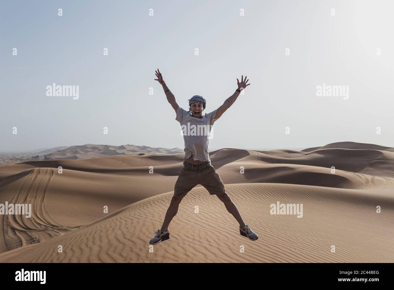 Excited male tourist jumping on sand dunes in desert at Dubai, United