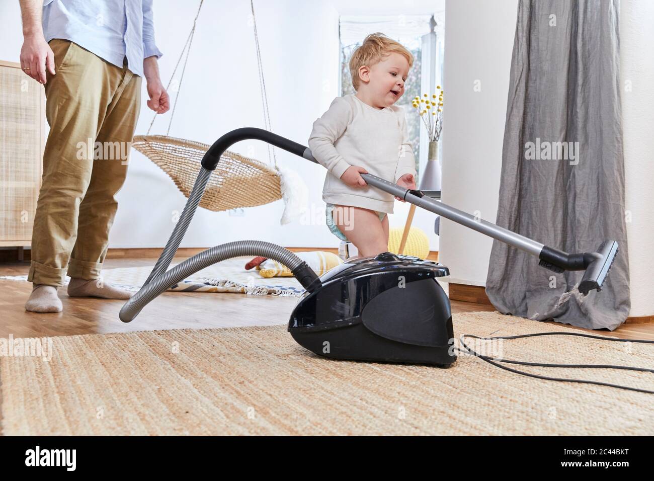Cute baby boy holding vacuum cleaner while standing on carpet by father