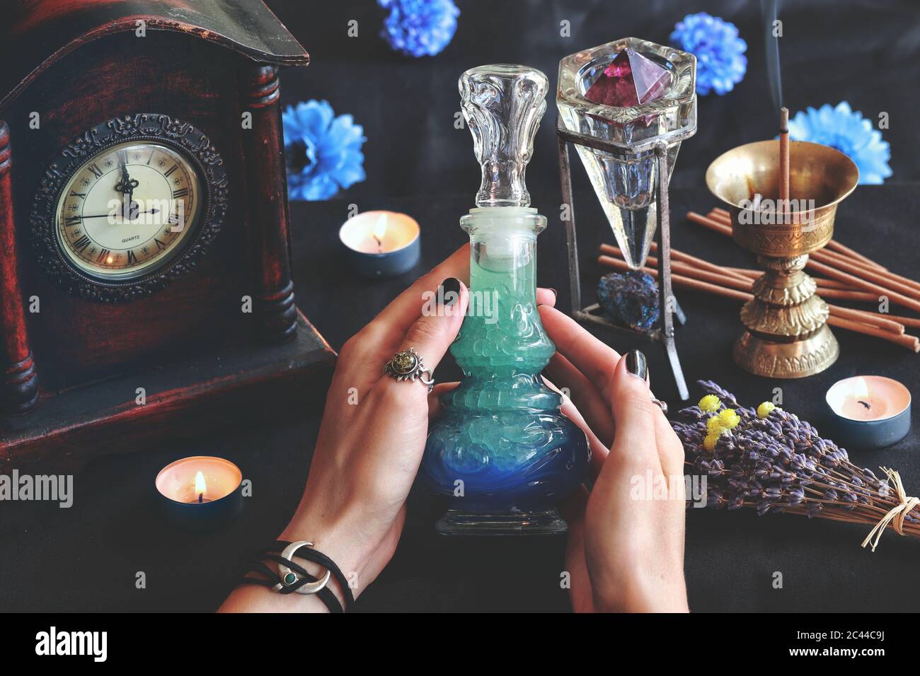 Wiccan witch holding a lucid dreaming good night potion in her hands at her altar. Blue colored liquid in a beautiful vintage potion bottle Stock Photo