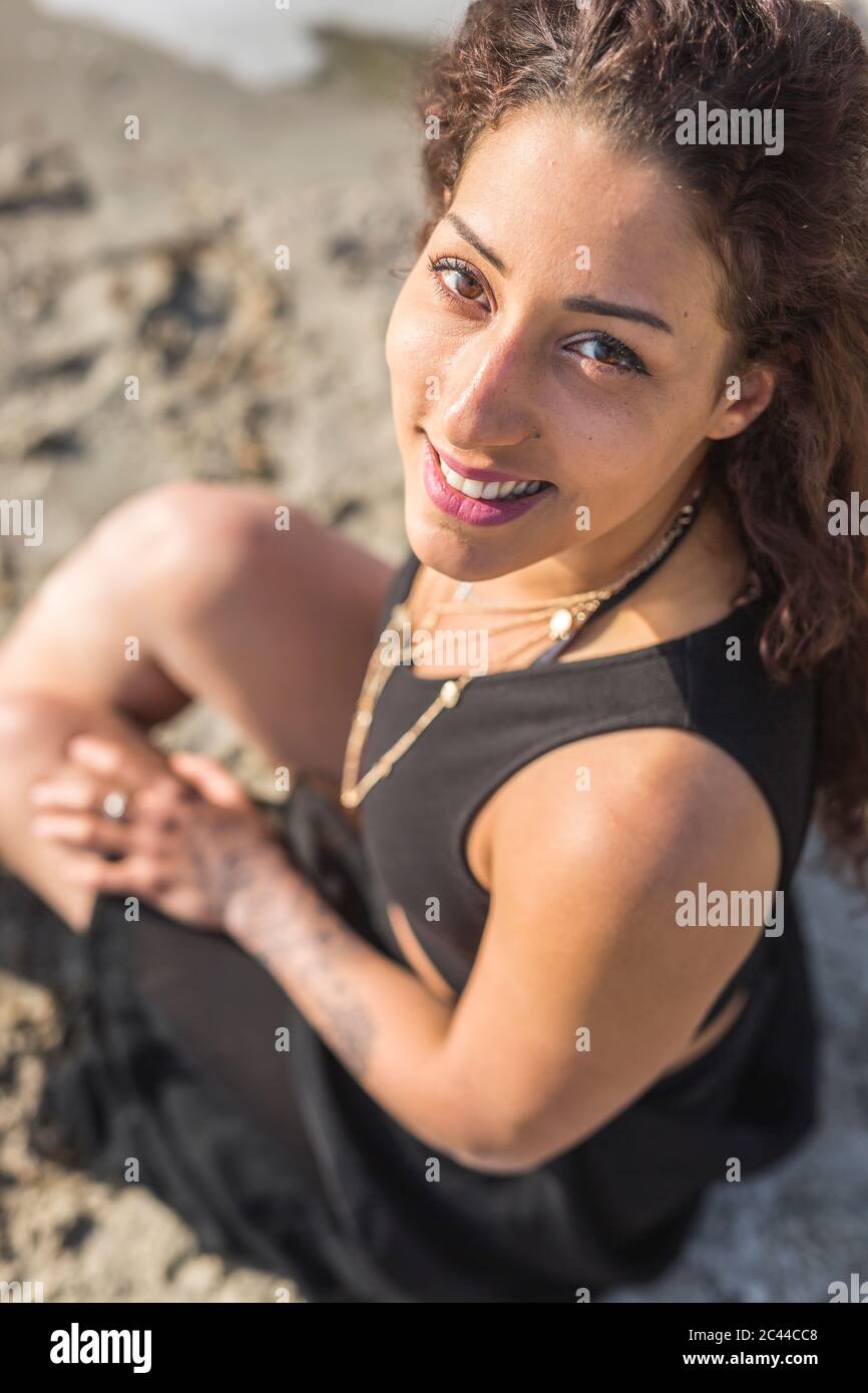 Portrait of smiling young woman sitting on the beach Stock Photo - Alamy