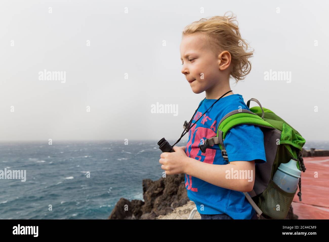 Boy with binoculars and backpack looking at sea while standing at Costa Adeje, Canary Islands, Spain Stock Photo