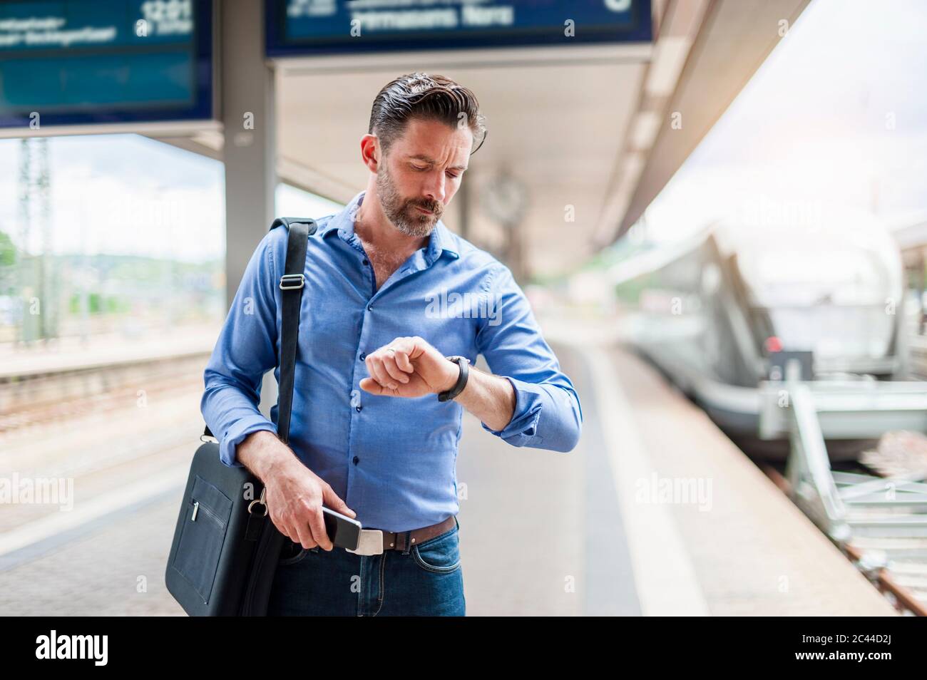 Bearded commuter looking at wristwatch while standing railroad station platform Stock Photo