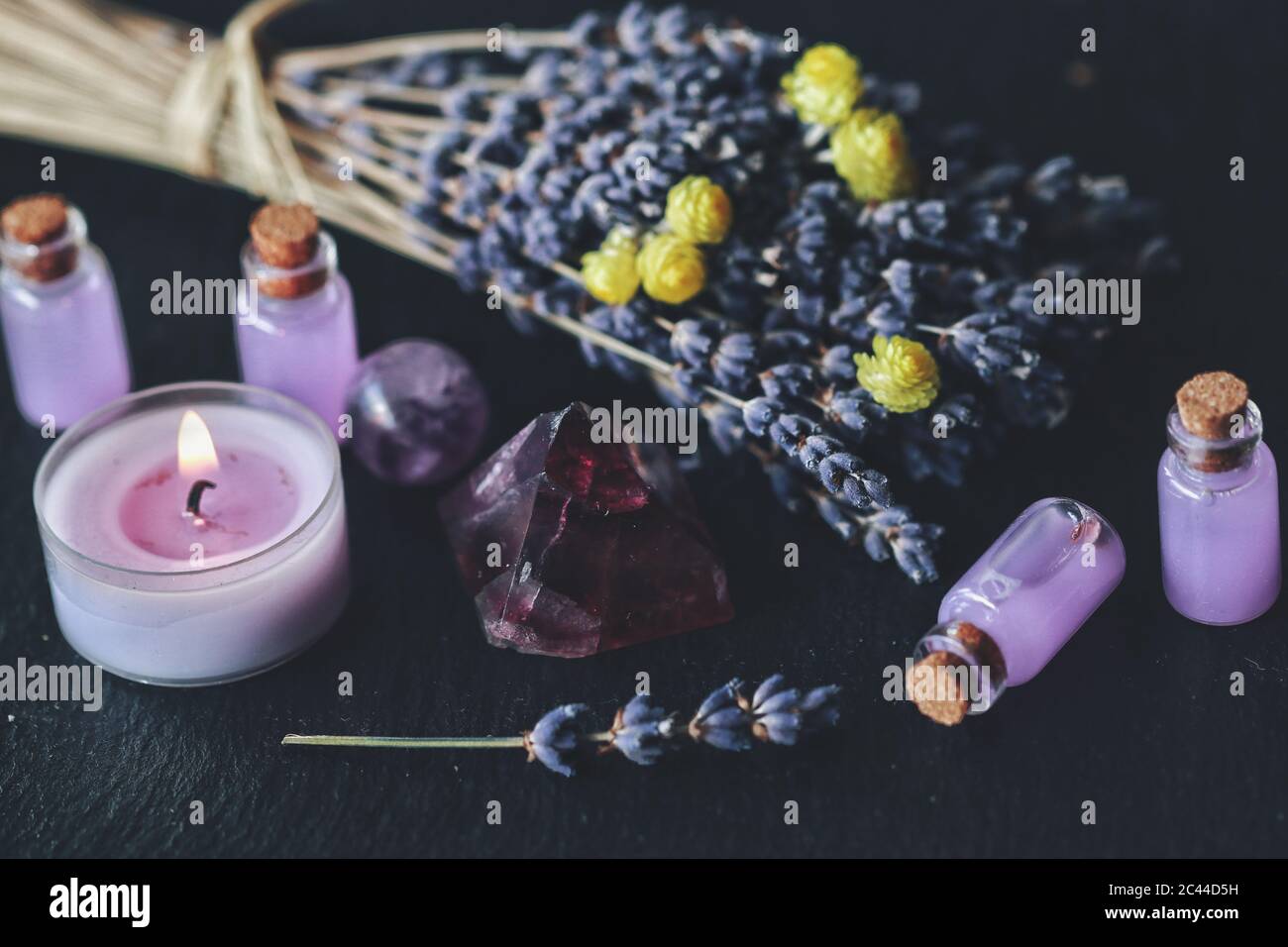 Herbal magick in wicca and witchcraft using lavender infused water. Purple lit burning candle, amethyst pyramid crystal, dried lavender flowers Stock Photo