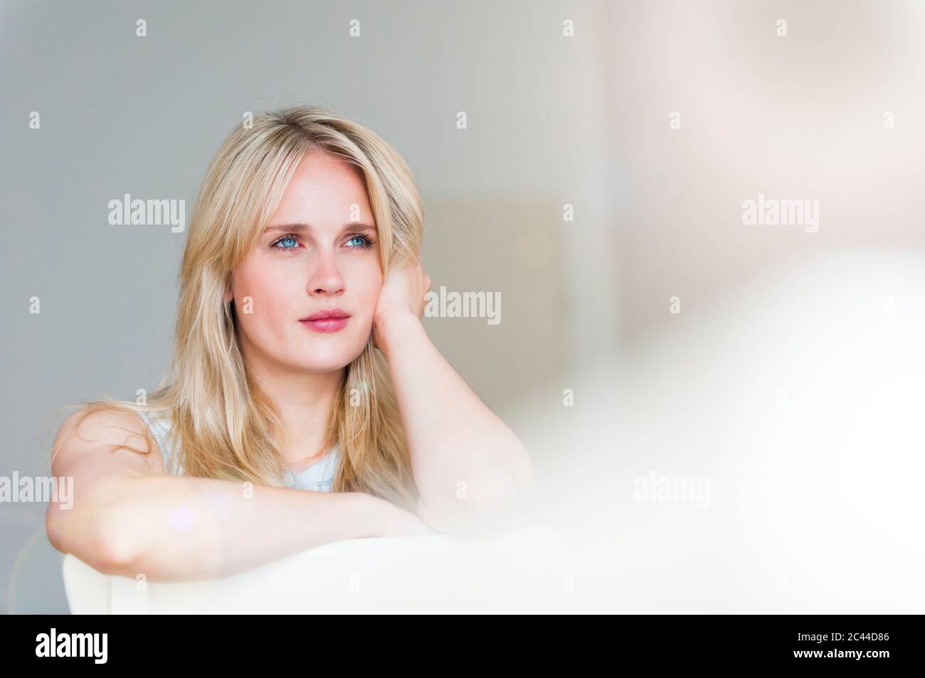 Portrait of pensive blond woman with blue eyes leaning on back rest Stock Photo