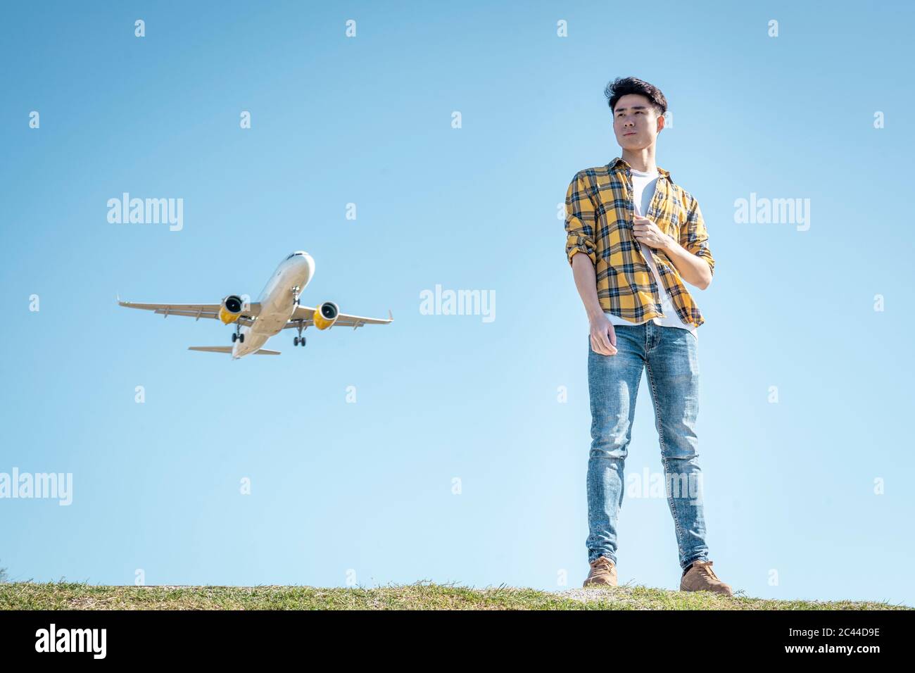 Portrait of young man standing on a hill looking at distance with airplane above him Stock Photo