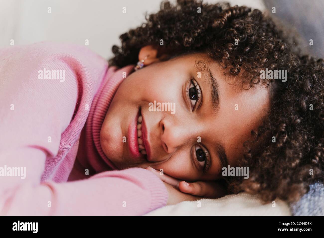 Portrait of smiling little girl wearing pink turtleneck pullover lying on couch Stock Photo