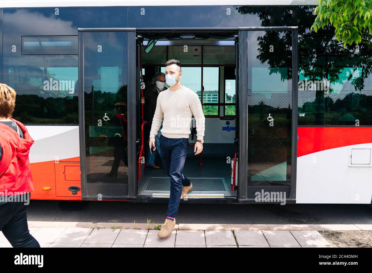 Young man wearing protective mask getting off public bus hires stock