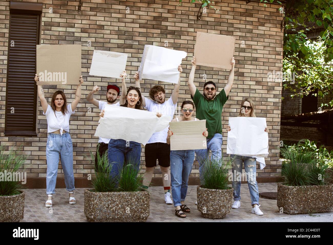 Diverse group of people protesting with blank sign. Protest against human rights, abuse of freedom, social issues, actual problems. Men and women on the street look angry, screaming. Copyspace. Stock Photo