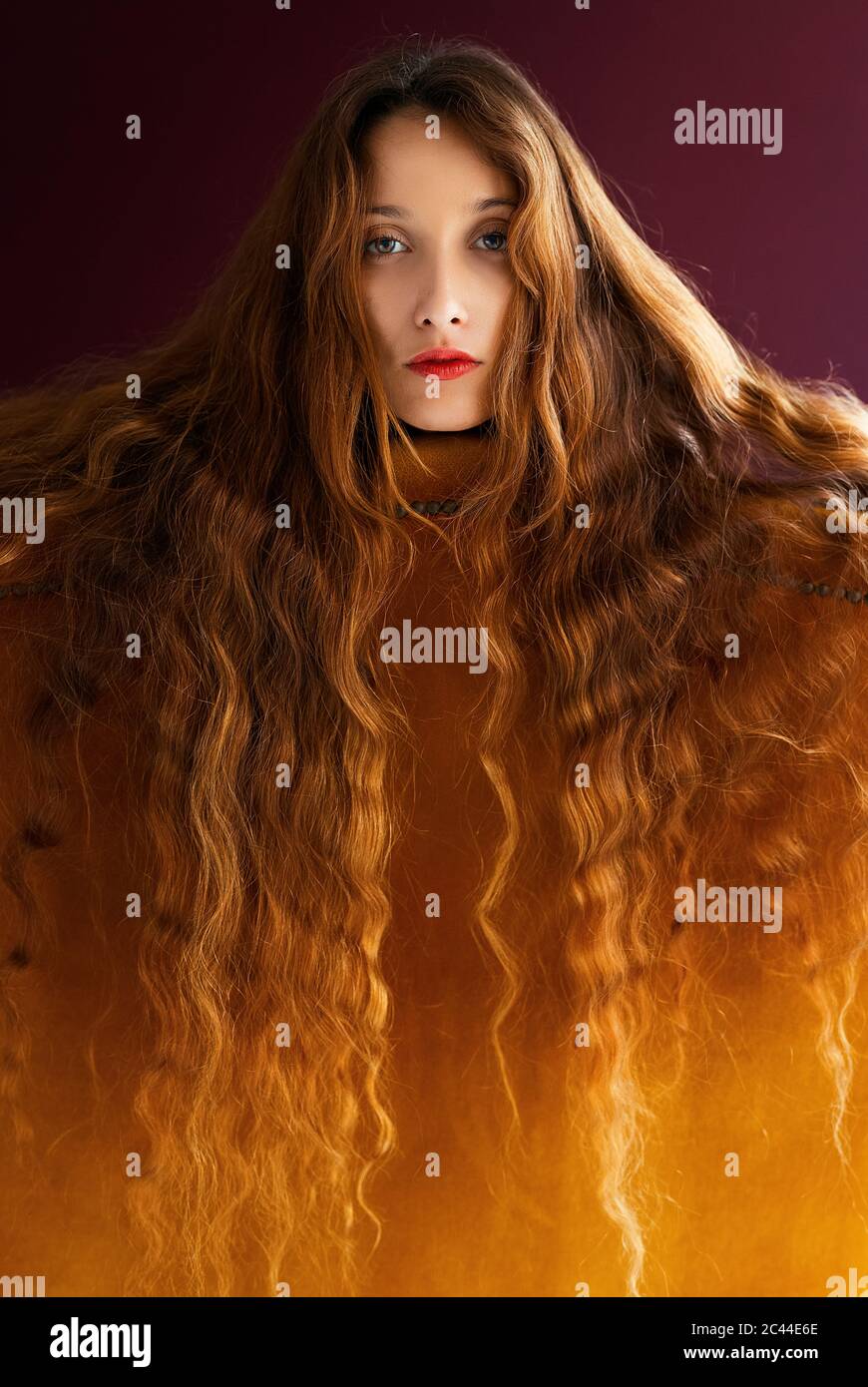 Portrait of young woman with long brown wavy hair leaning on golden chair against colored background Stock Photo