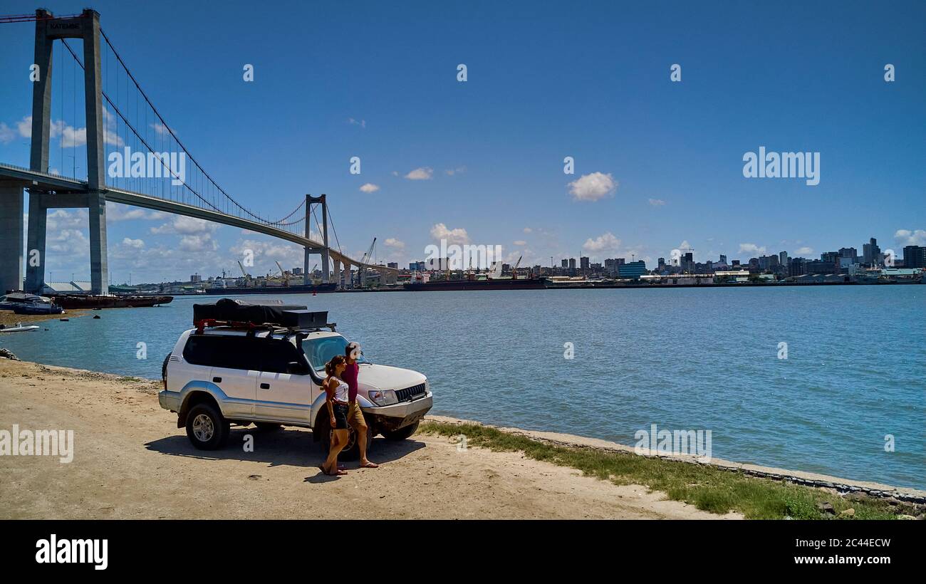 Mozambique, Katembe, Adult couple standing by 4x4 car admiring view of Maputo Bay with city and Maputo-Katembe Bridge in background Stock Photo