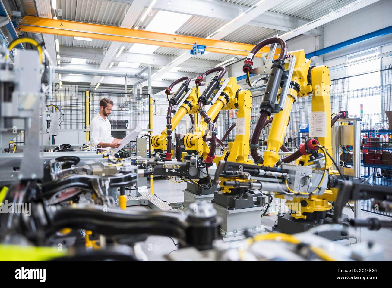 Young engineer reading paper while standing by robotic arms in automated industry Stock Photo