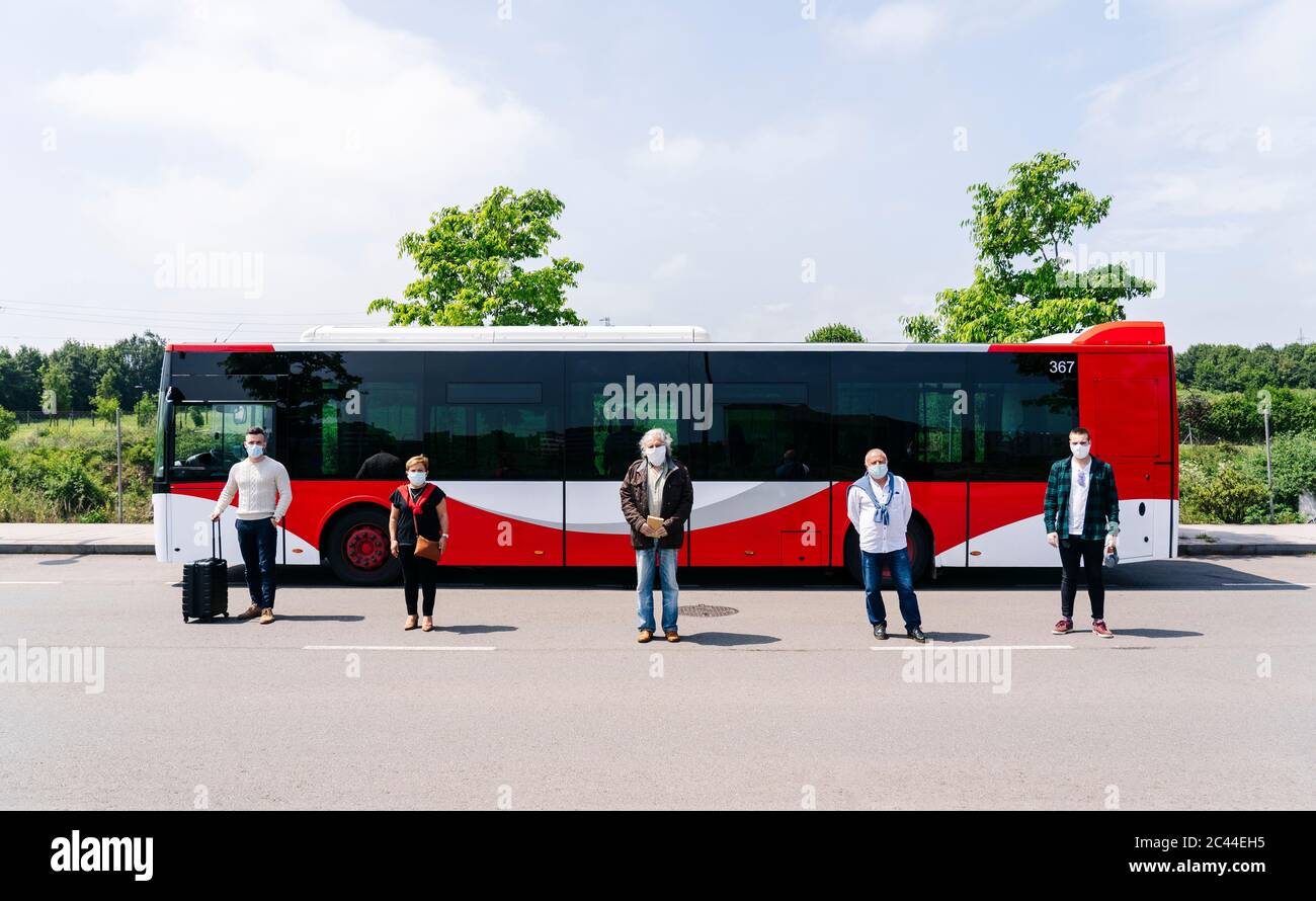 Five passengers wearing protective masks standing in a row in front of public bus, Spain Stock Photo