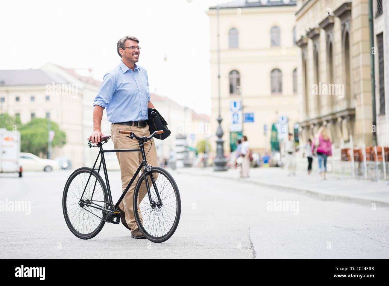 Smiling businessman looking away while walking with bicycle on road in city Stock Photo