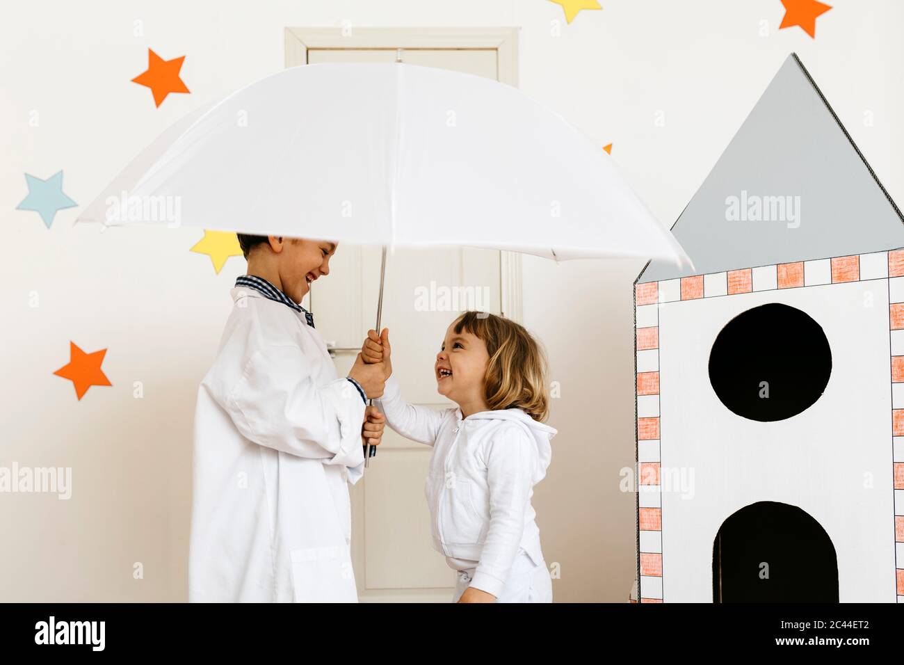 Siblings playing astronaut and researcher with umbrella at rocket Stock Photo