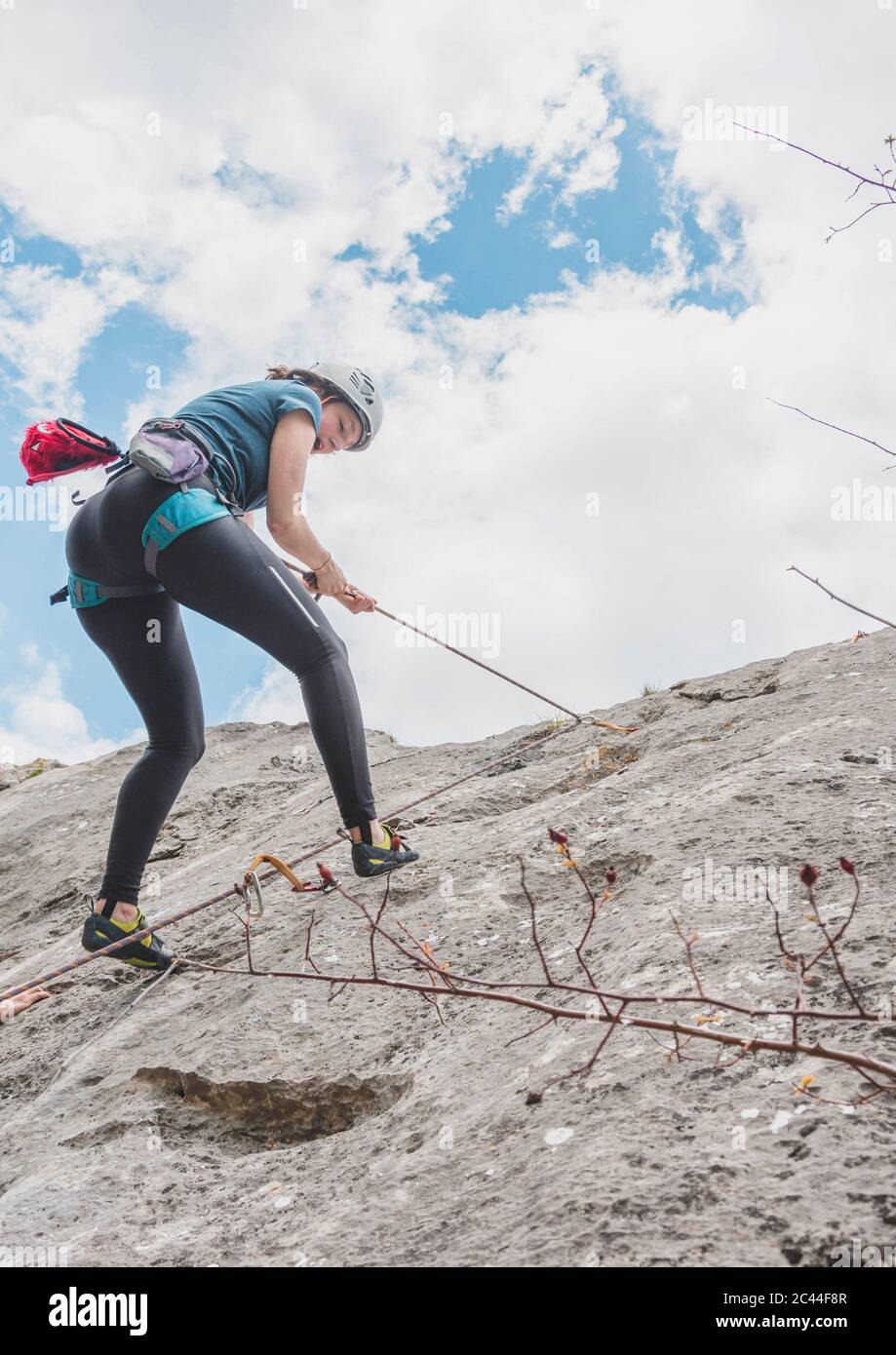 Young woman rappelling down with rope on rock against sky Stock Photo