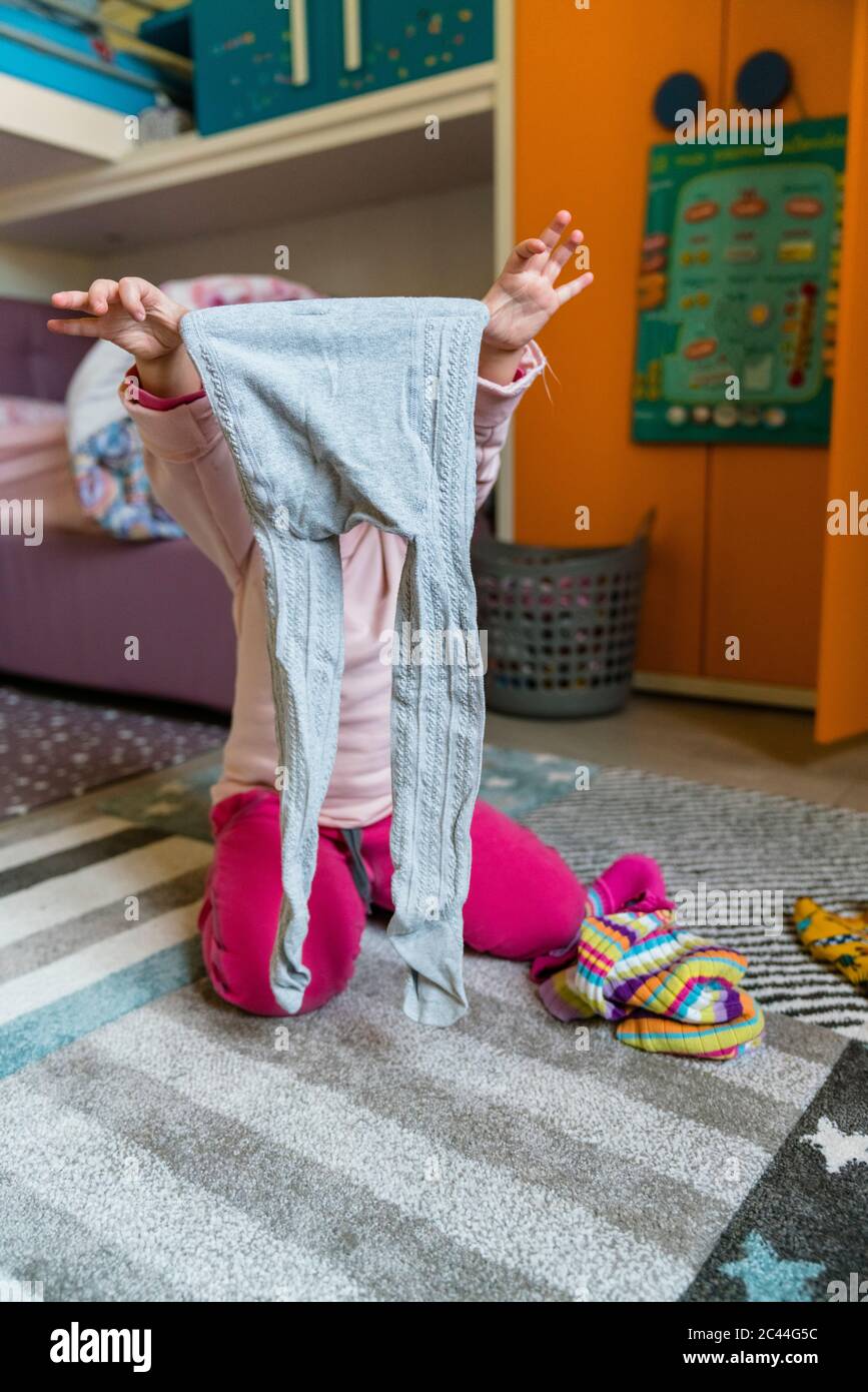 Preschool girl holding leggings while kneeling on carpet in bedroom at home Stock Photo
