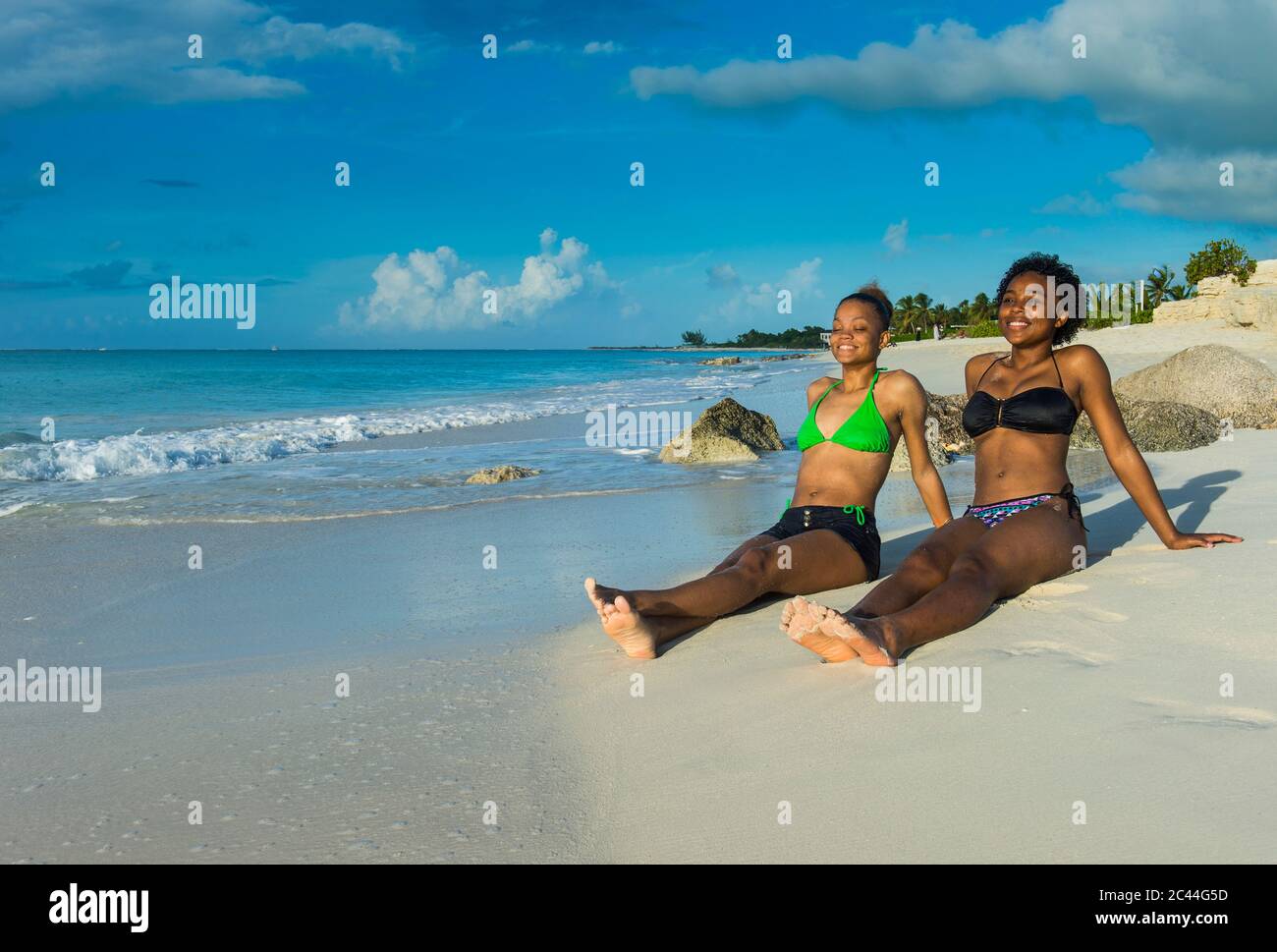 Smiling female friends wearing bikinis relaxing at Grace Bay beach during sunset, Providenciales, Turks And Caicos Islands Stock Photo