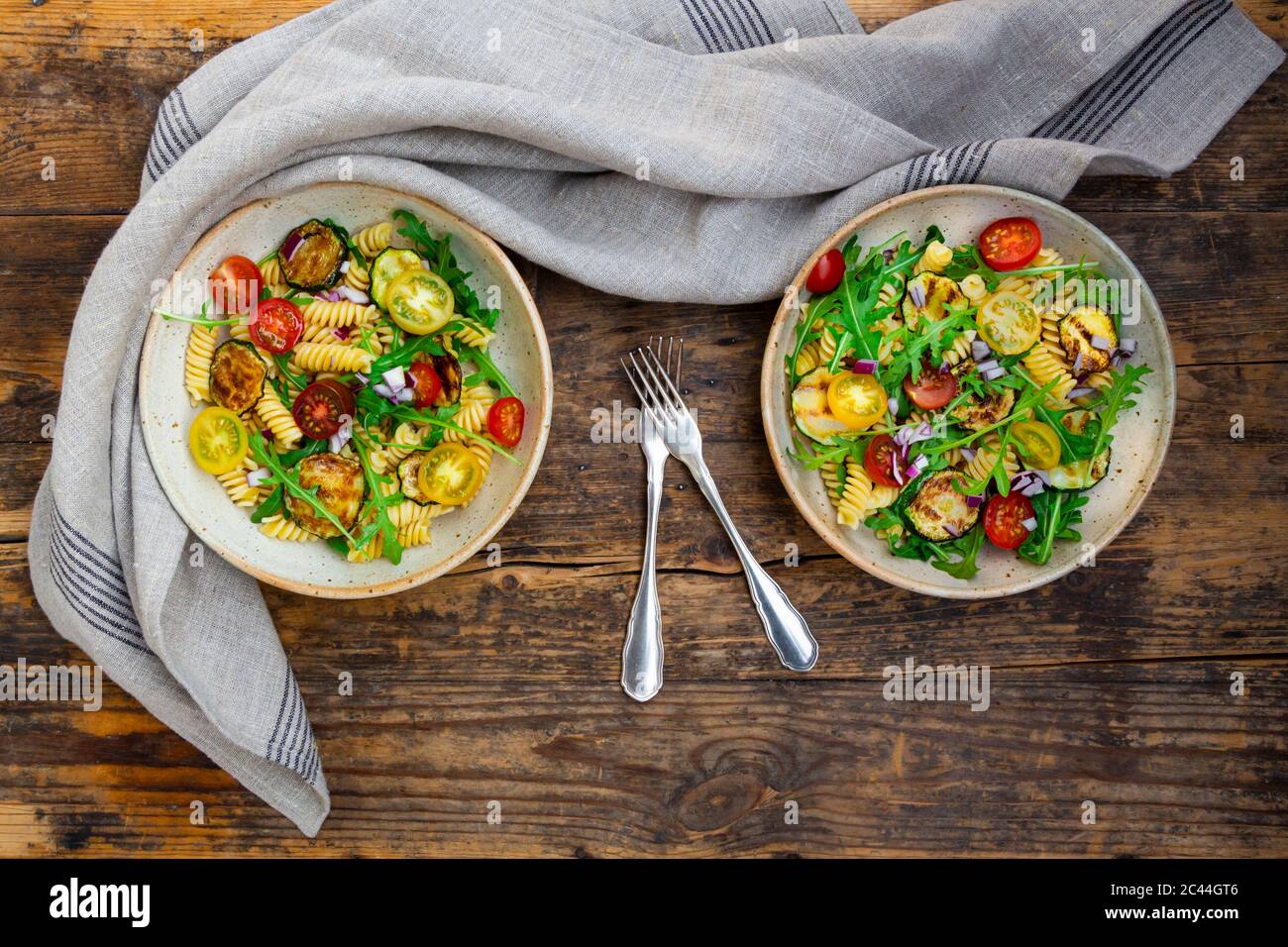 Two bowls of pasta salad with grilled zucchini, tomatoes, arugula, Spanish onion and balsamic vinegar Stock Photo