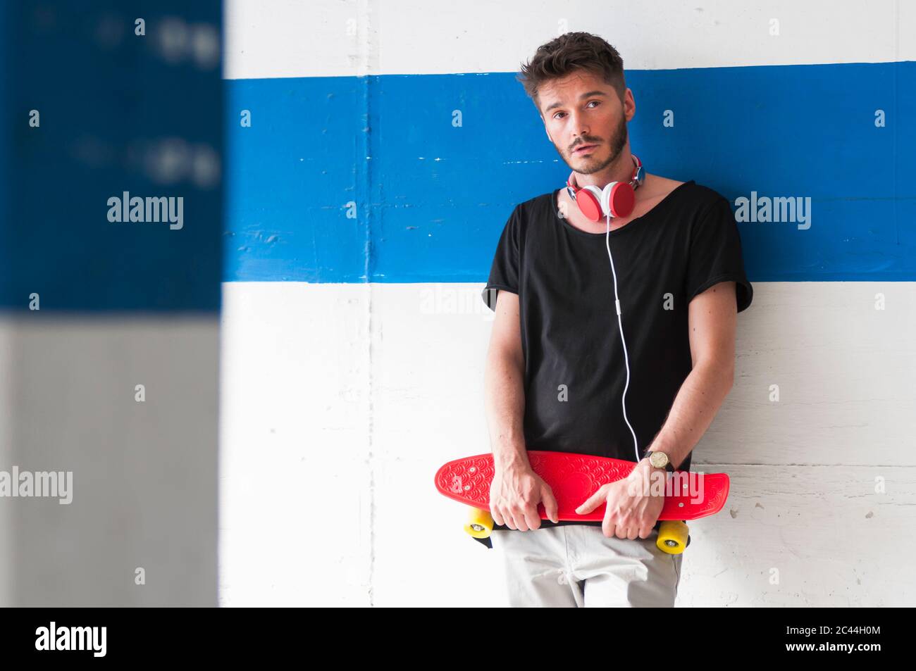 Portrait of man with skateboard leaning against wall Stock Photo Alamy