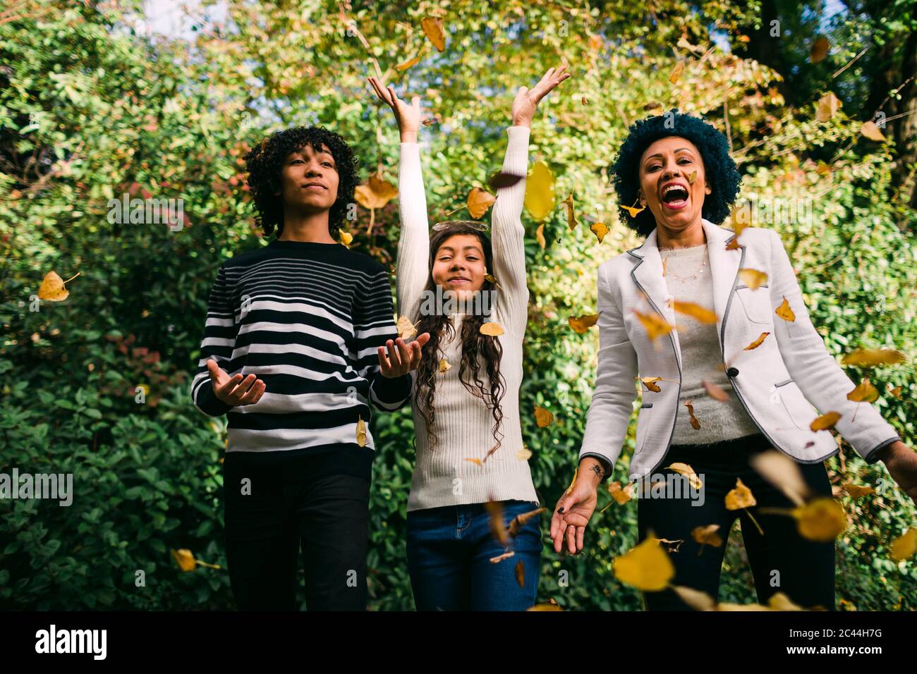 Happy children with mother throwing autumn leaves in park Stock Photo