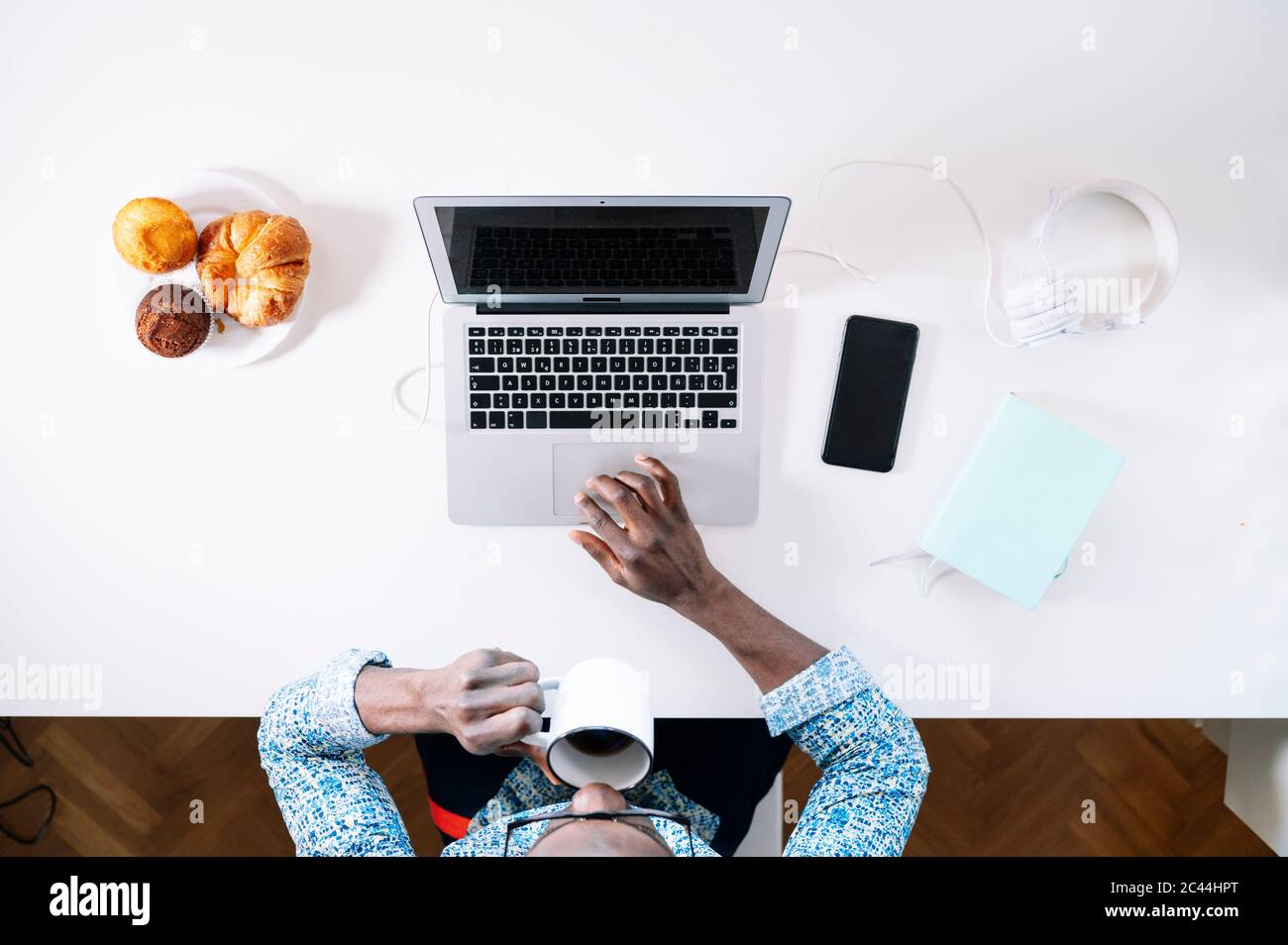 Young man drinking coffee while using laptop at home office desk Stock Photo