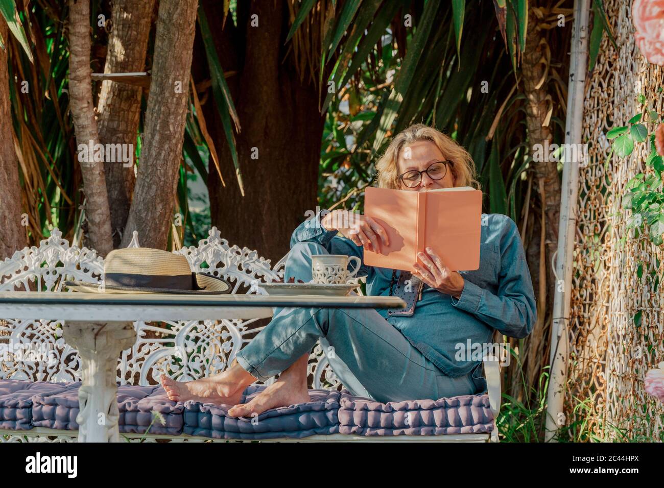 Senior woman sitting on garden bench reading a book Stock Photo - Alamy