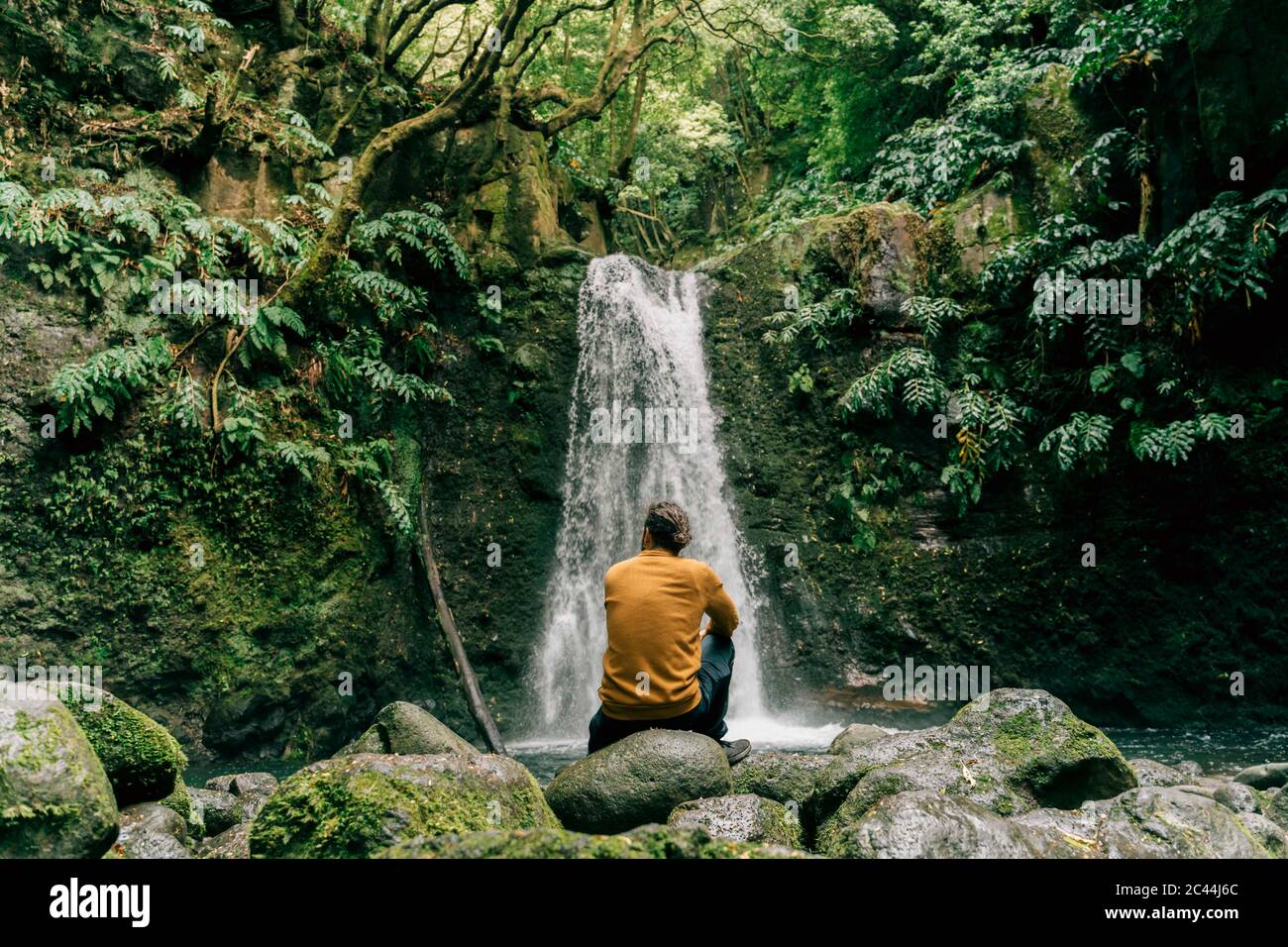 Rear view of man sitting at a waterfall on Sao Miguel Island, Azores, Portugal Stock Photo