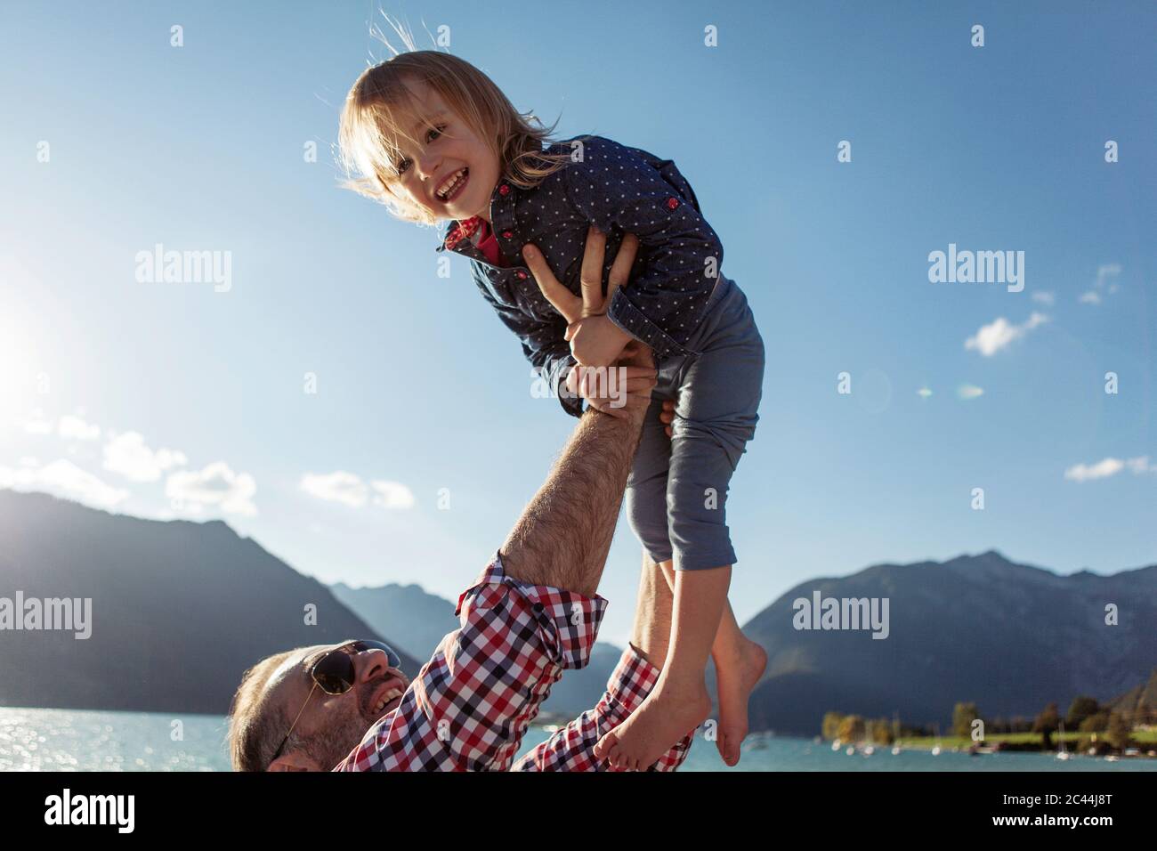 Father holding aloft cheerful daughter against blue sky at Achensee, Tyrol State, Austria Stock Photo
