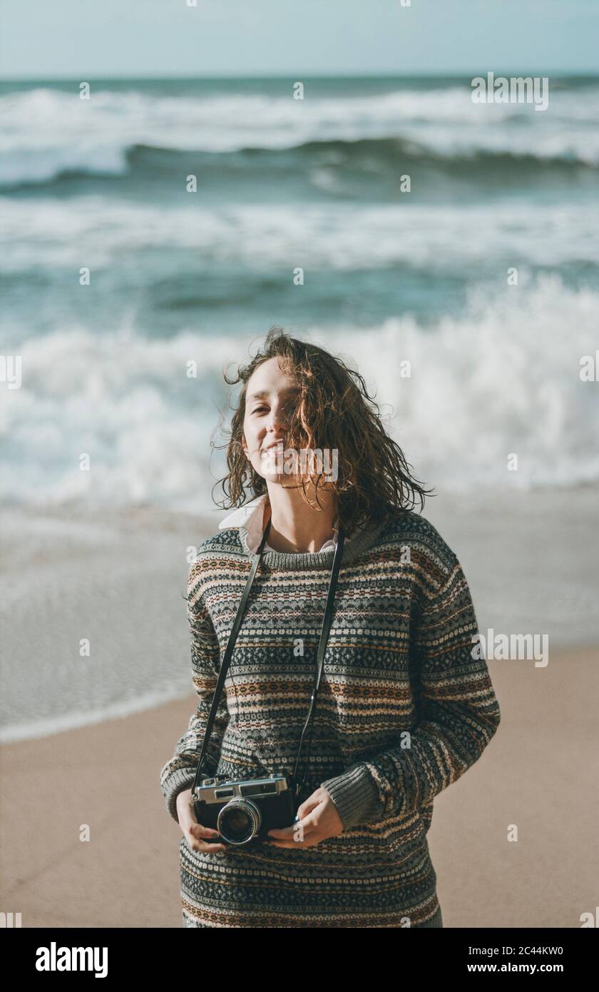 Beautiful young woman standing with camera at beach, Praia da Ursa ...