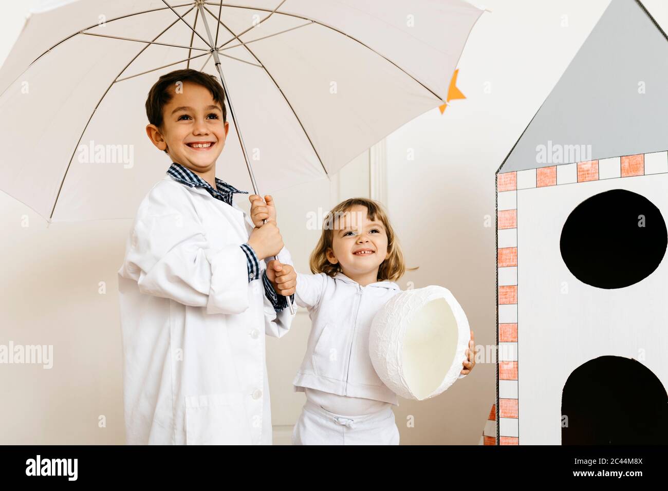 Siblings playing astronaut and researcher with umbrella at rocket Stock Photo