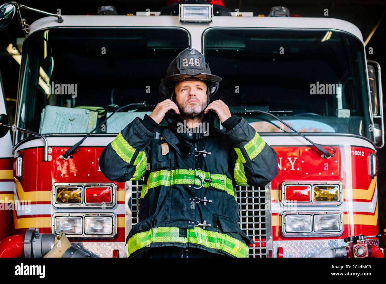 USA, New York, Portrait of firefighter putting on helmet in front of fire engine Stock Photo