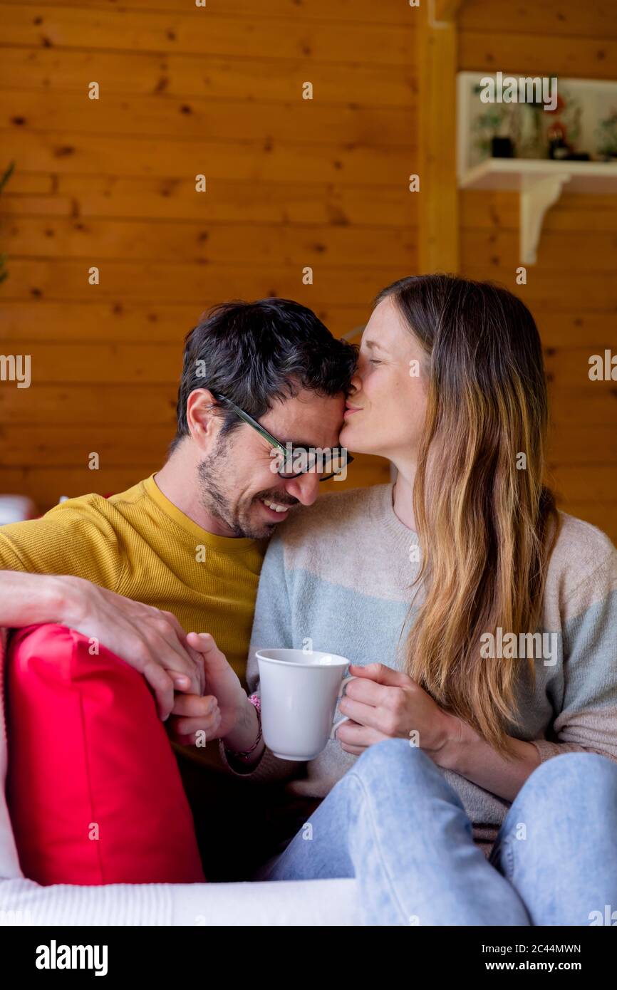 Loving woman kissing on man forehead while relaxing in log cabin Stock Photo