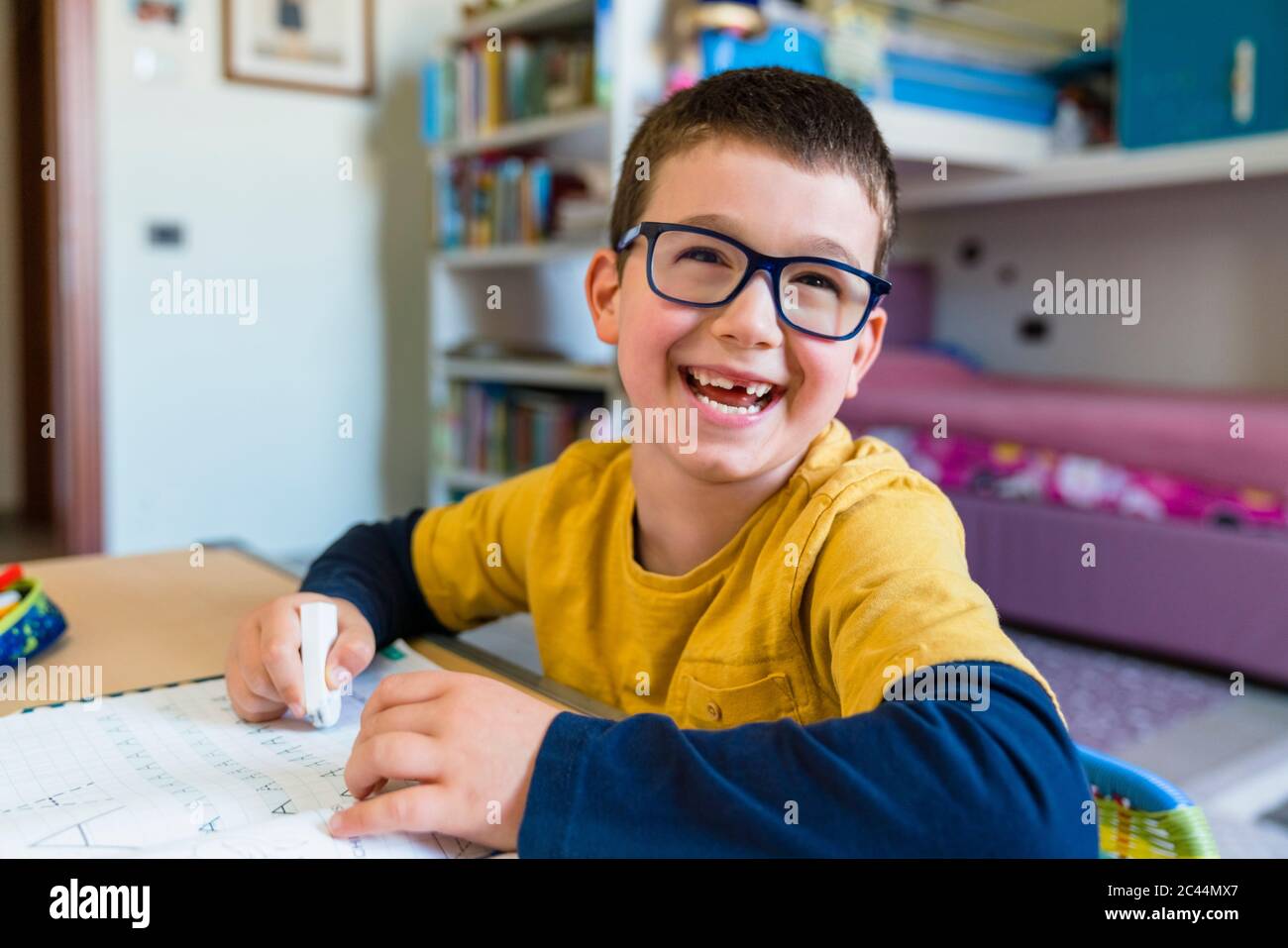 Cheerful cute student sitting with book at desk during pandemic outbreak Stock Photo