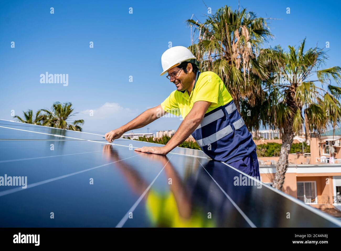 Smiling mature technician installing solar panel on house roof against blue sky Stock Photo