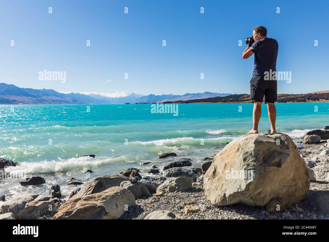 New Zealand, Oceania, South Island, Canterbury, Ben Ohau, Lake Pukaki and Southern Alps (New Zealand Alps) with Aoraki / Mount Cook, Man standing on boulder and photographing landscape Stock Photo