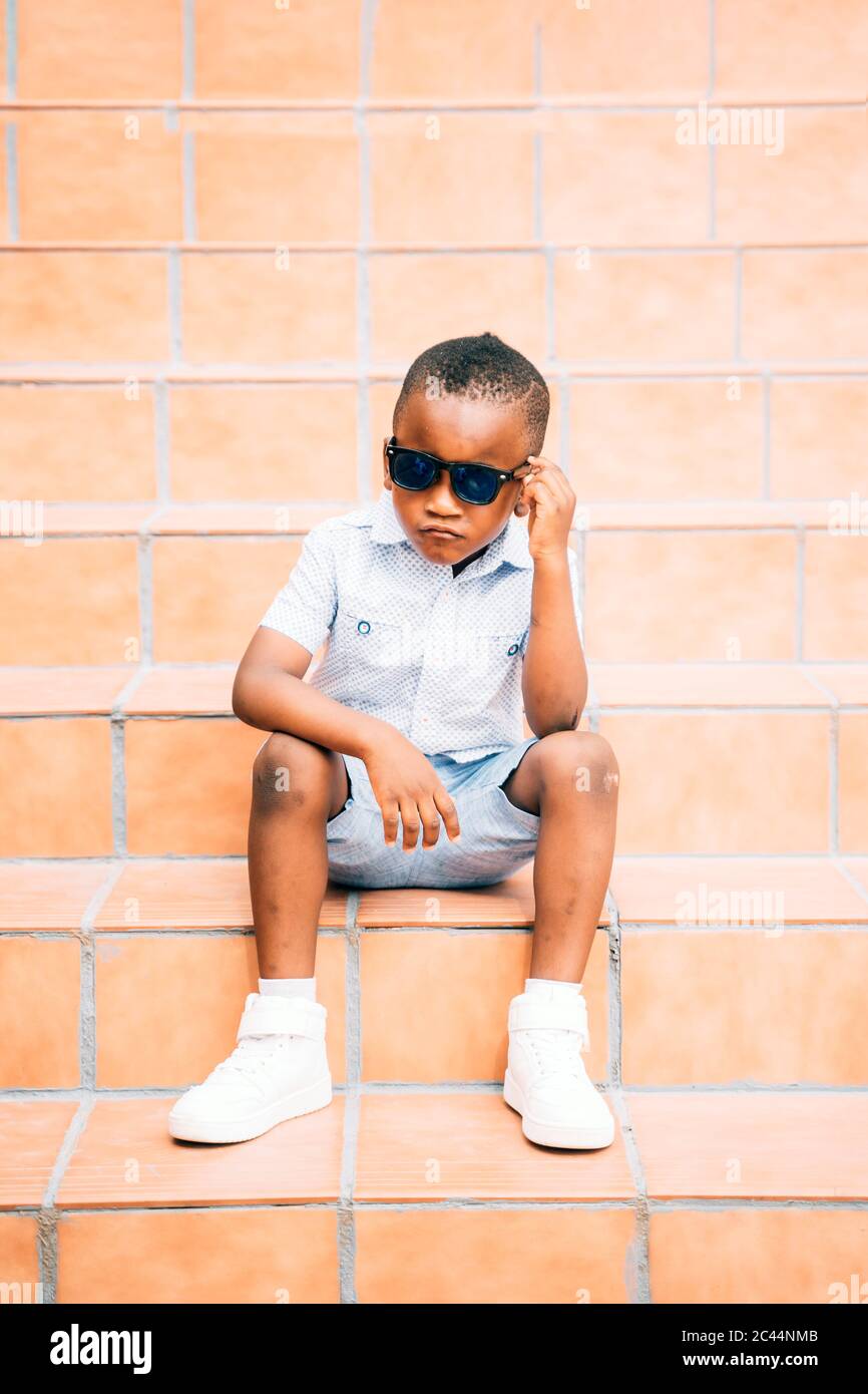Portrait of cool little boy wearing sunglasses sitting on stairs outdoors Stock Photo