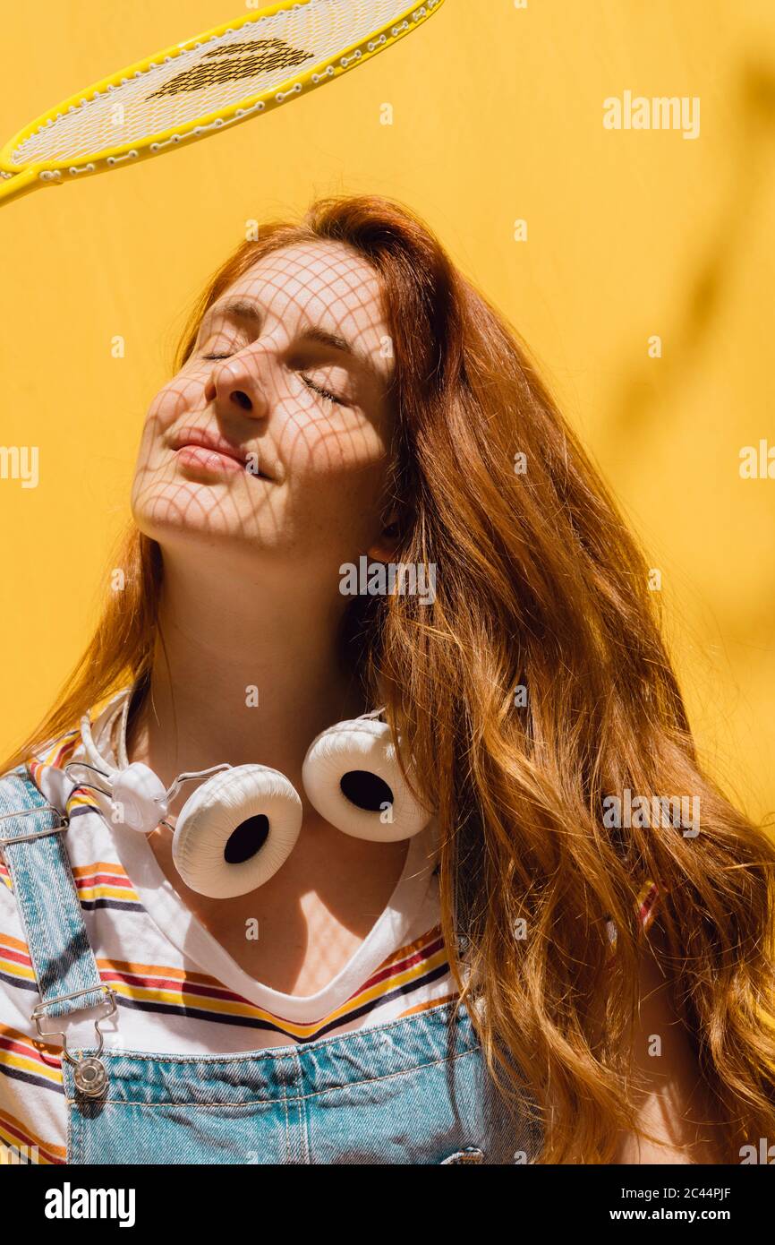 Relaxed young woman with badminton racket over face wearing headphones around neck during sunny day Stock Photo