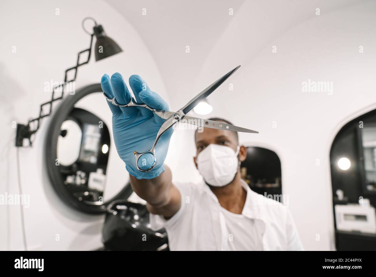 Barber wearing surgical mask and reusable gloves holding scissors Stock Photo