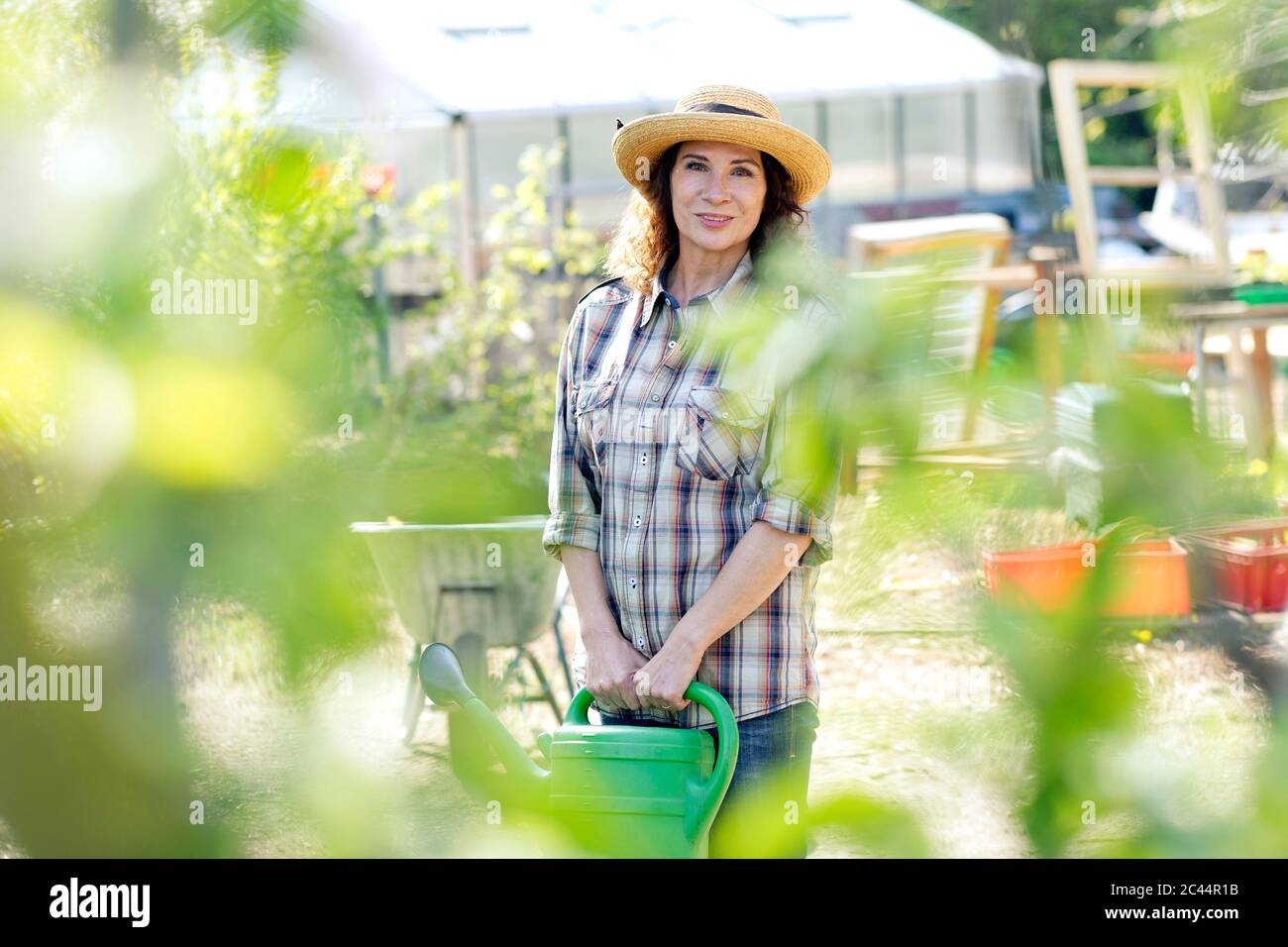 Portrait of smiling female farmer holding watering can while standing ...