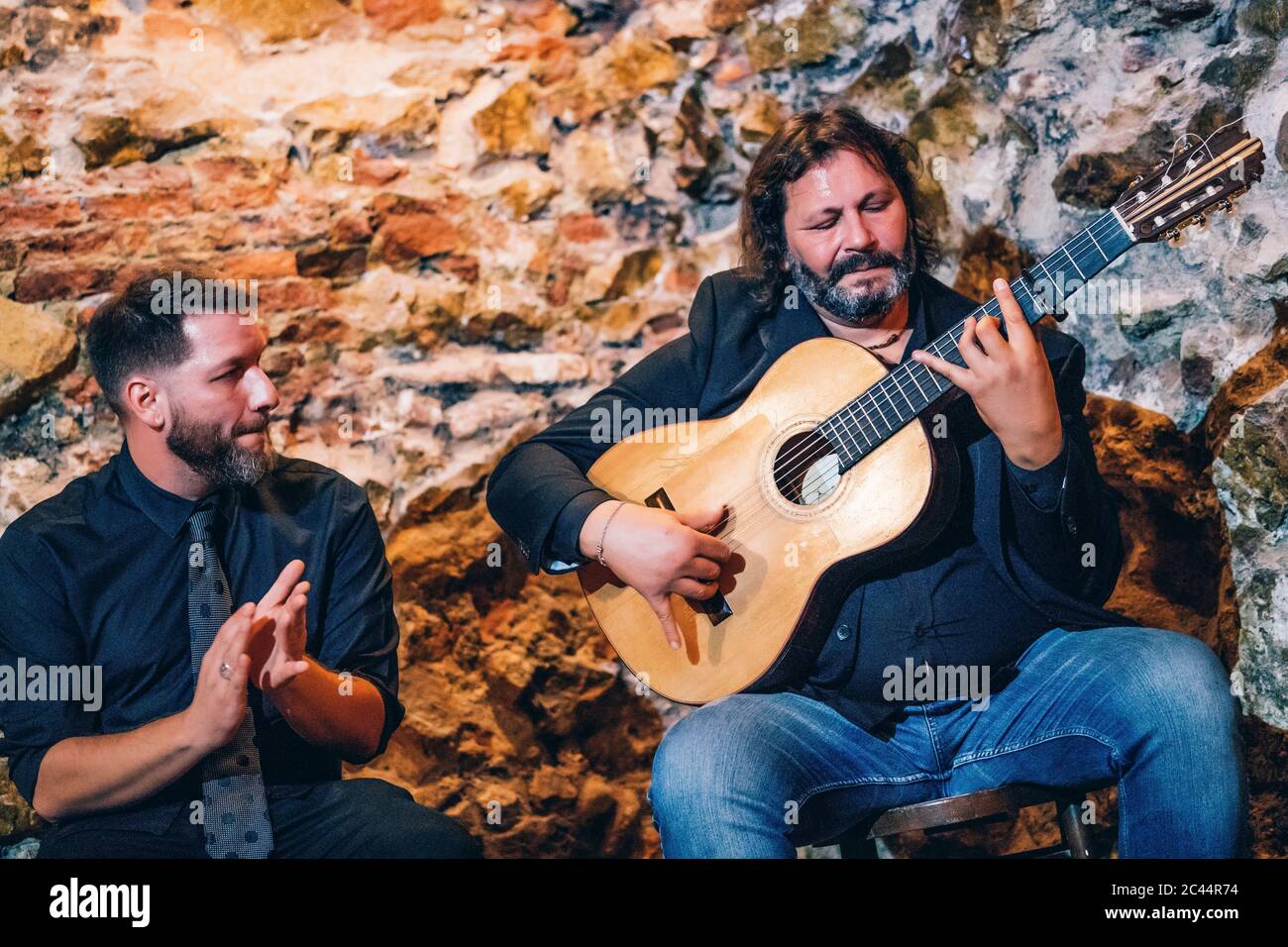 Singer clapping hands while man playing flamenco on guitar against wall in club Stock Photo
