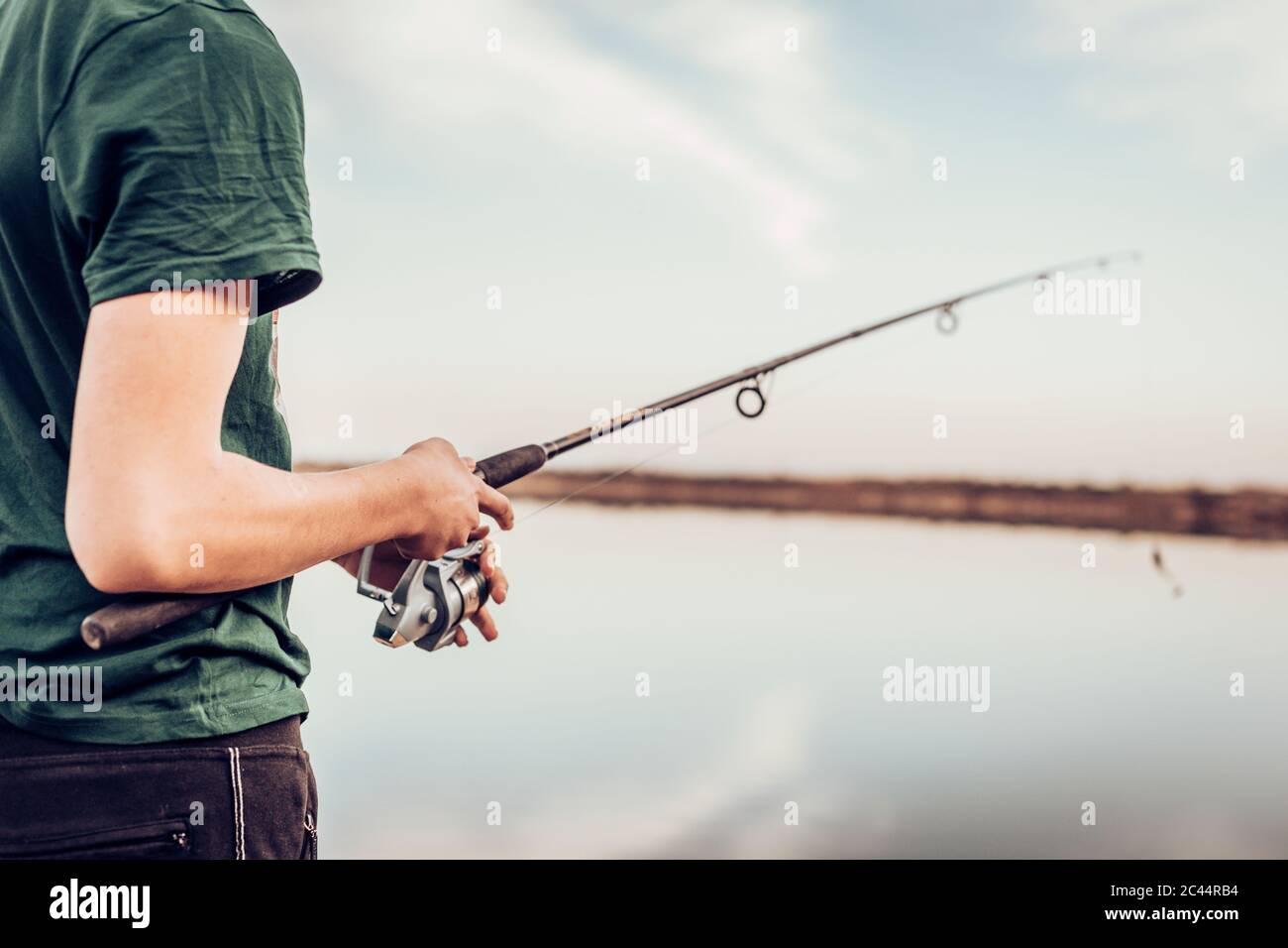 Midsection of teenage boy fishing with rod in lake while standing against cloudy sky Stock Photo